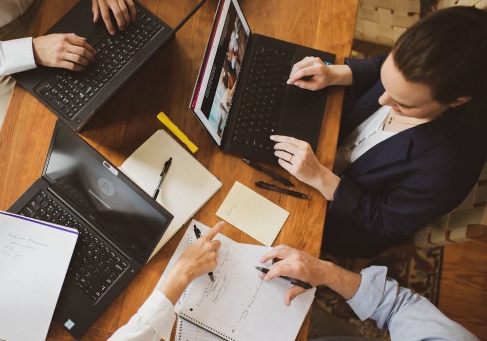 Vista cenital de cuatro personas trabajando con notebooks y cuadernos sobre una mesa de madera